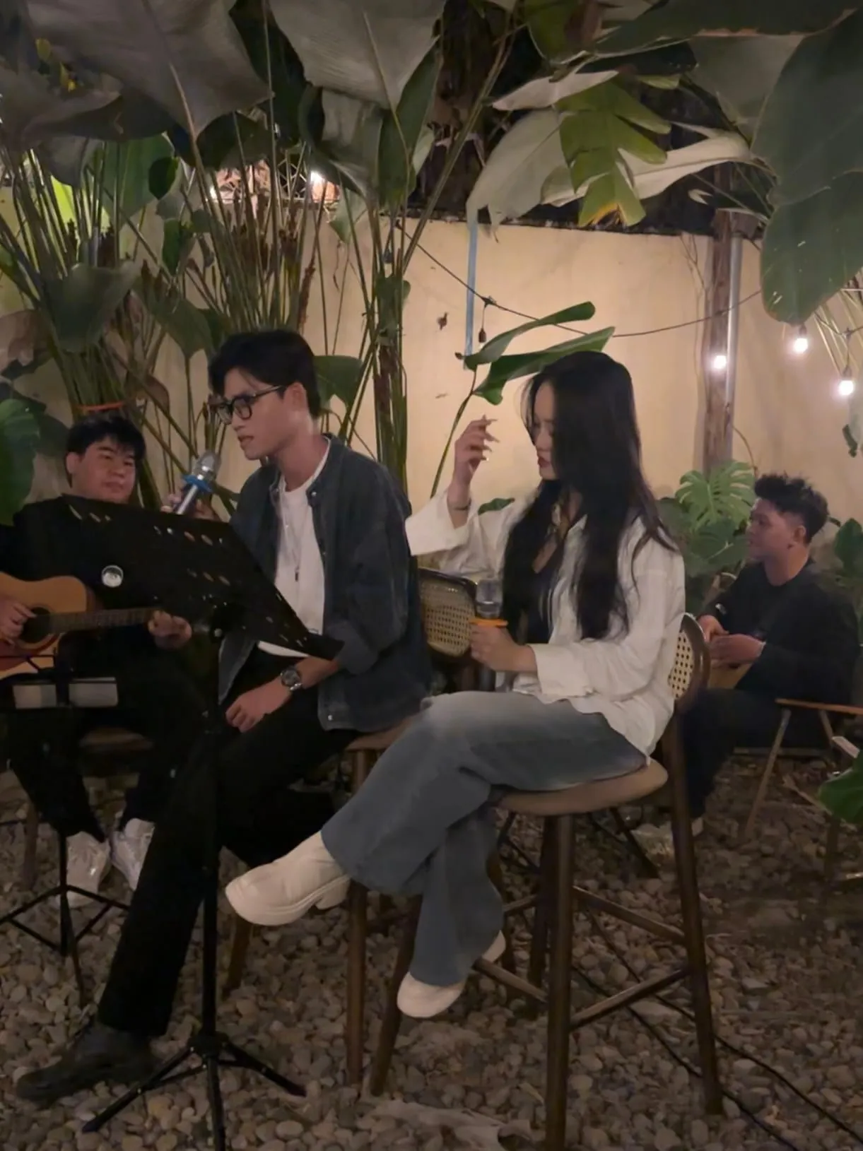 Đôi ca sĩ ngồi hát bên guitarist giữa góc vườn buổi tối